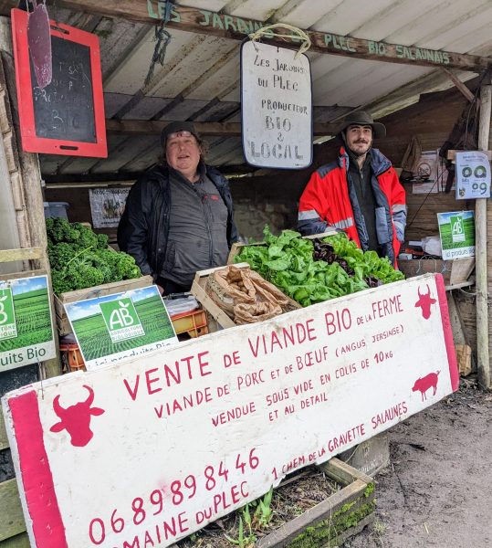 Deux hommes devant leur stand de fruits et légume à la ferme