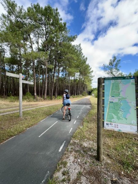 Cycliste de dos regardant un panneau directionnel « Lacanau Océan » sur la Vélodyssée, au cœur de la forêt médocaine
